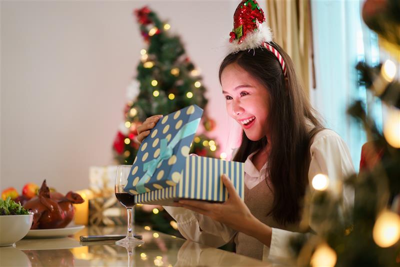 Asian woman smiling as she opens a Christmas gift